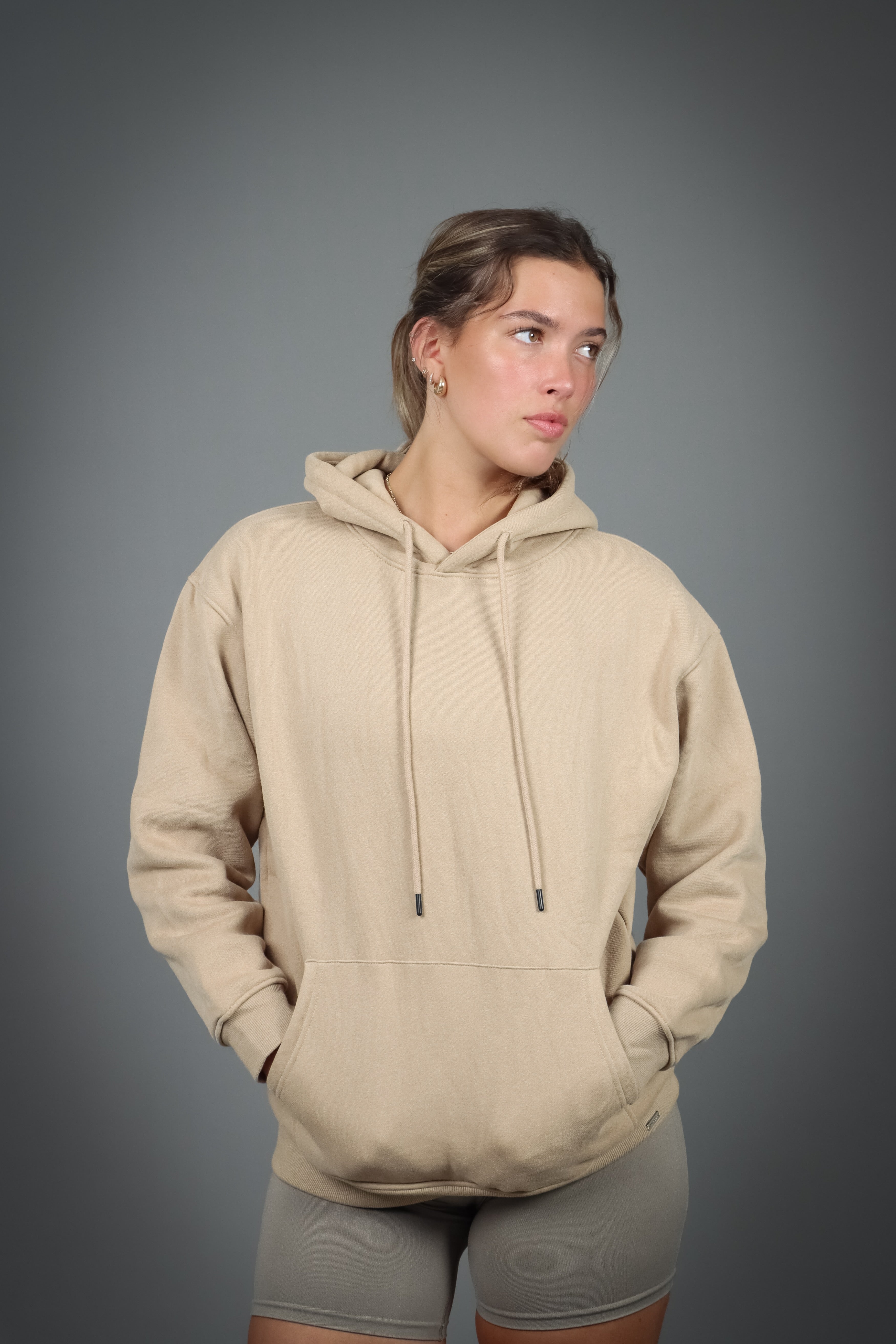 Aurora Hoodie Beige, en blød og behagelig hættetrøje med justerbar hætte og diskret metallogo, perfekt til både stil og komfort på kølige dage