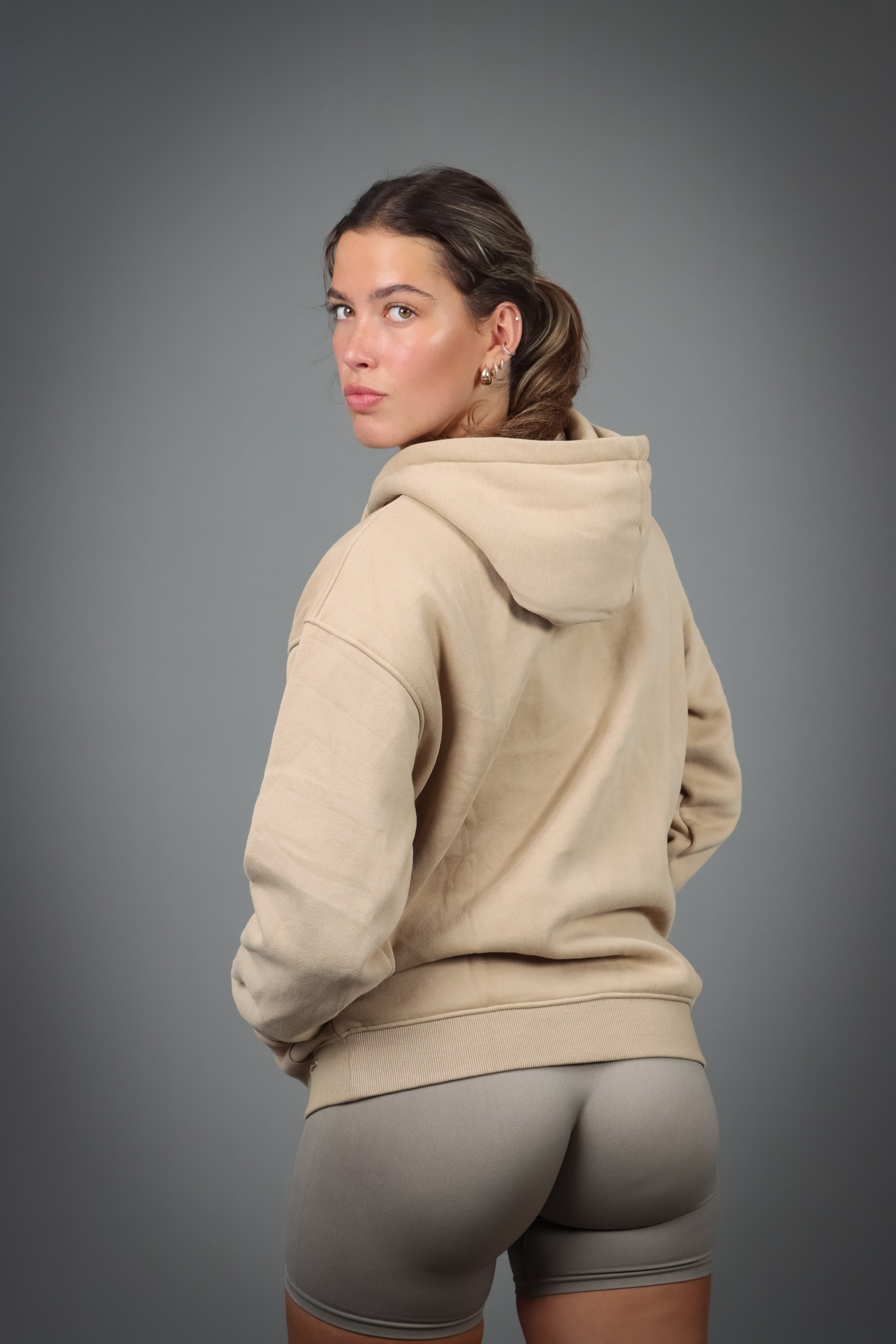 Aurora Hoodie Beige, en blød og behagelig hættetrøje med justerbar hætte og diskret metallogo, perfekt til både stil og komfort på kølige dage