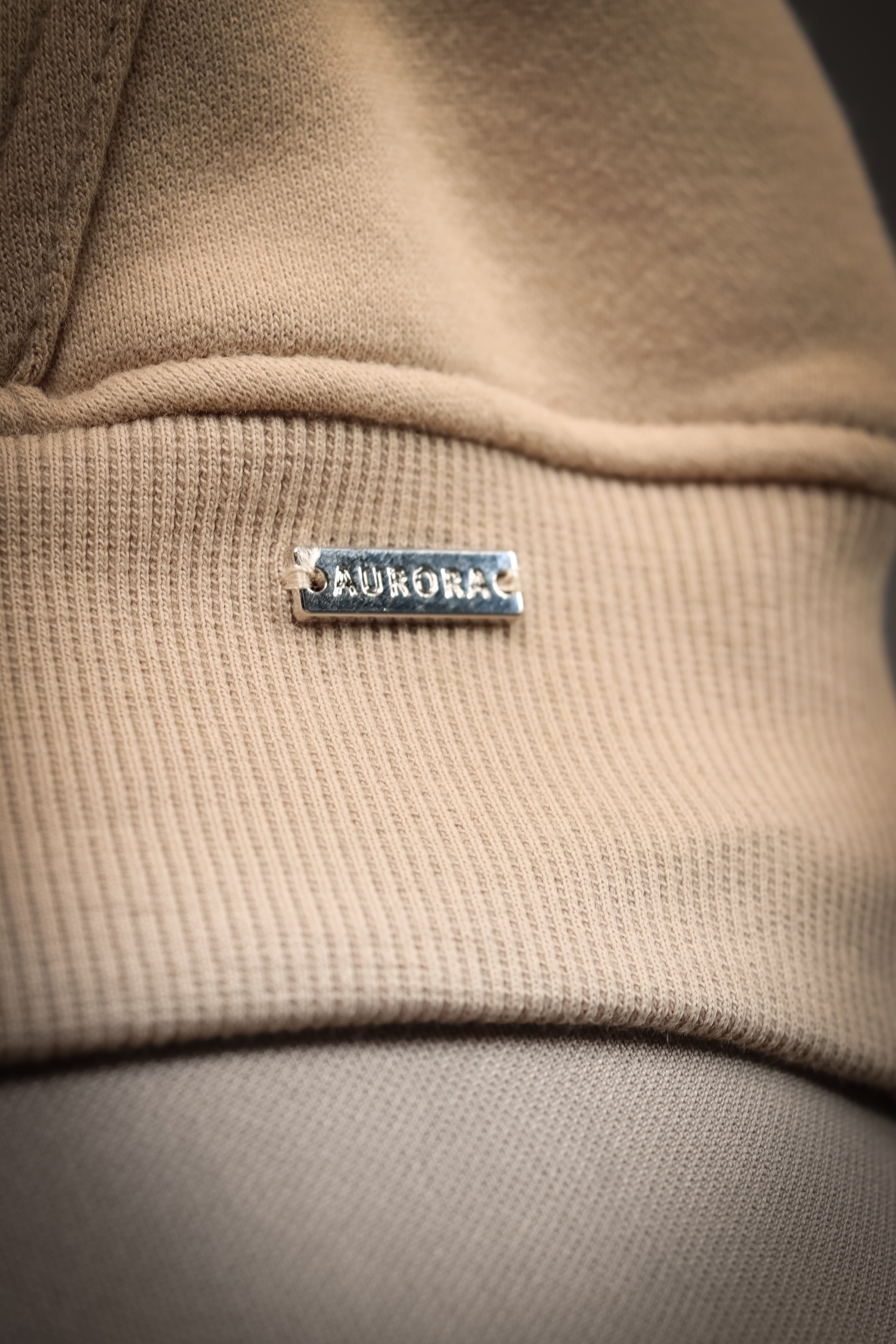 Aurora Hoodie Beige, en blød og behagelig hættetrøje med justerbar hætte og diskret metallogo, perfekt til både stil og komfort på kølige dage